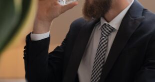 Bearded businessman wearing glasses, drinking water in modern office.