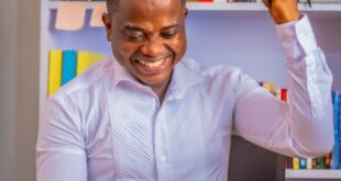 African man celebrating success on mobile phone in a vibrant home office.