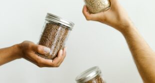 Four hands holding glass jars of grains and legumes, emphasizing kitchen organization.