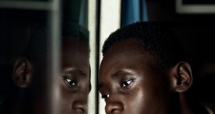 A young man deep in thought, reflecting on a bus window in Ghana.