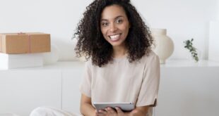 A confident young woman sitting among packages and papers while using a tablet, showcasing modern entrepreneurship.
