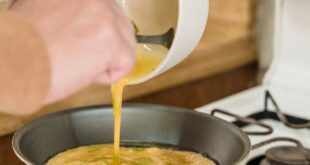 Person making an omelet in a frying pan over a gas stove indoors, showcasing cooking process.