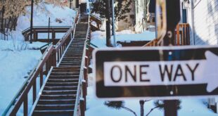 Snow-covered staircase leading uphill with a visible one-way sign in a winter cityscape.
