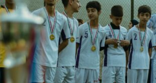 Teenage soccer team in Erbil celebrating victory with medals on outdoor field.