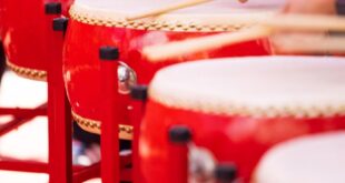 A row of drummers energetically playing red Chinese drums during a cultural celebration.