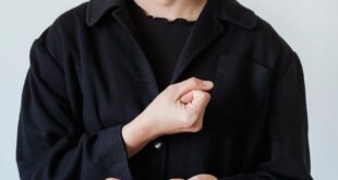 Asian woman using American Sign Language with a smile, wearing a black jacket.