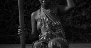 Black and white full body of African barefoot female in traditional clothes sitting with old utensil