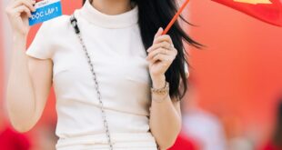 Smiling woman holding Vietnam flag and ticket, celebrating National Day outdoors.
