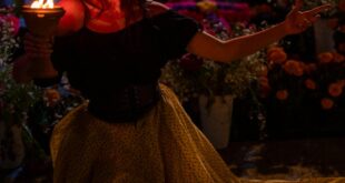 A woman in traditional makeup and costume celebrates Dia de los Muertos at night.