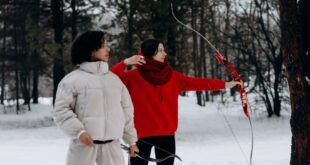 Two individuals practicing archery in a snowy forest environment, showcasing winter sports activity.