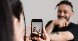 A woman records a man while making a TikTok video indoors, highlighting creativity and social media interaction.