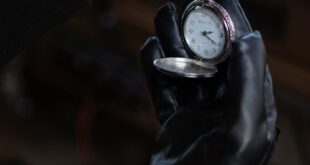 A leather-gloved hand holding an antique pocket watch, evoking nostalgia and elegance.
