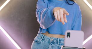 Asian woman streaming content using smartphone and tripod in modern setup.