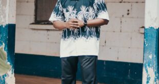 Man wearing sunglasses and tropical shirt standing outdoors next to weathered building.