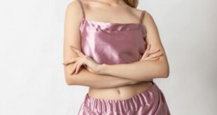 Portrait of a young woman in pink silk pajamas against a white background. Stylish and modern sleepwear fashion.