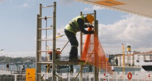 Construction worker securing safety net on scaffold at outdoor site.