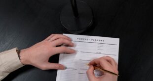 Top view of a person writing in a podcast planner near a microphone.