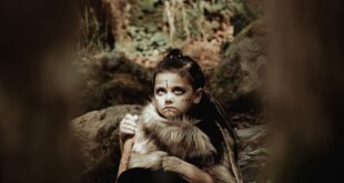 Child dressed as a warrior sitting in an enchanting forest scene.
