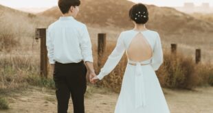 Rear view of a newlywed couple holding hands walking in an outdoor setting.