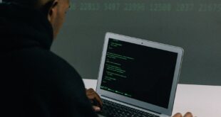 A programmer engaged in coding on a laptop in a tech-focused workspace with a digital interface.