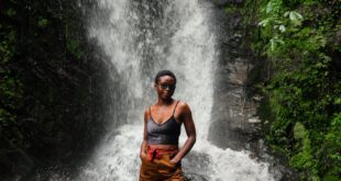 A woman stands confidently in front of a lush waterfall, embodying nature's adventure.