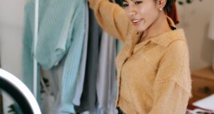 Young woman recording fashion content indoors with a smartphone and ring light.