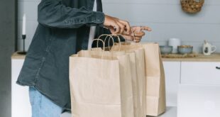 Young man organizing paper shopping bags indoors in a modern kitchen setting.